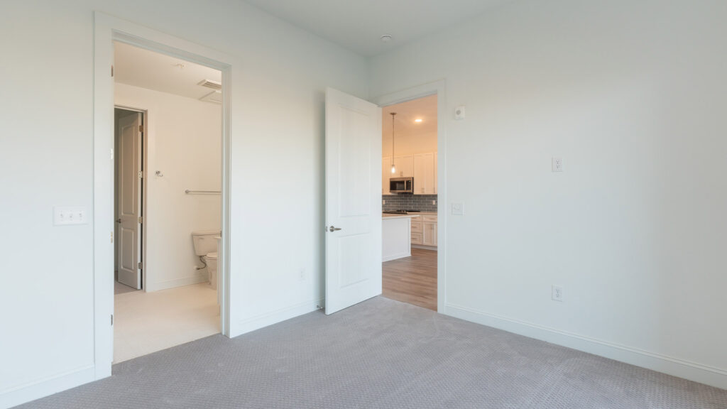 View from the bedroom of the kitchen at Cameryn Elise, luxury apartments for seniors, with blue colored tile backsplash, chandelier, kitchen island, stainless appliances